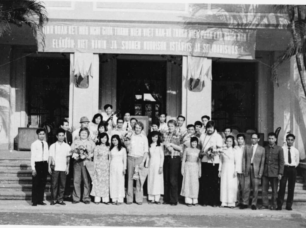 Suomalaisia valtion nuorisoneuvoston jäseniä vuonna 1974 ryhmäkuvassa isäntämaan osanottajien kanssa rakennuksen portaiden edessä. Taustalla roikkuu kangas, jossa kirjoitus: Eläköön Vietnamin ja Suomen nuorison ystävyys ja solidarisuus.
