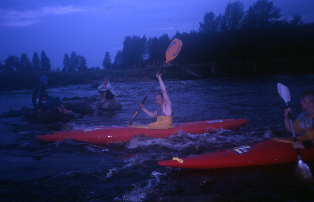 Neljä melojaa vuolaassa virrassa melomassa sinertävässä iltahämärässä.